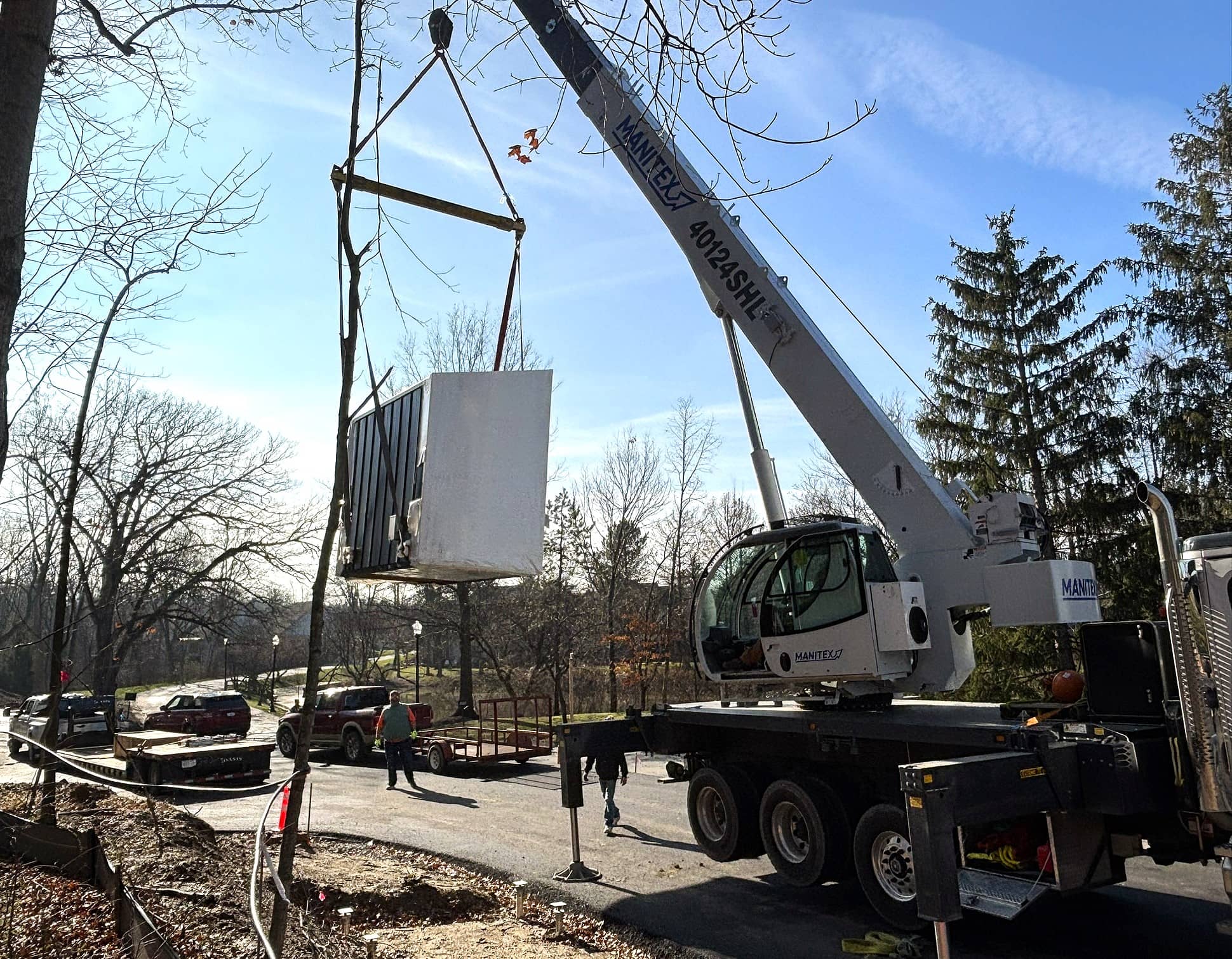 Crane lifting the prefabricated gatehouse above a wooded area during the installation process.