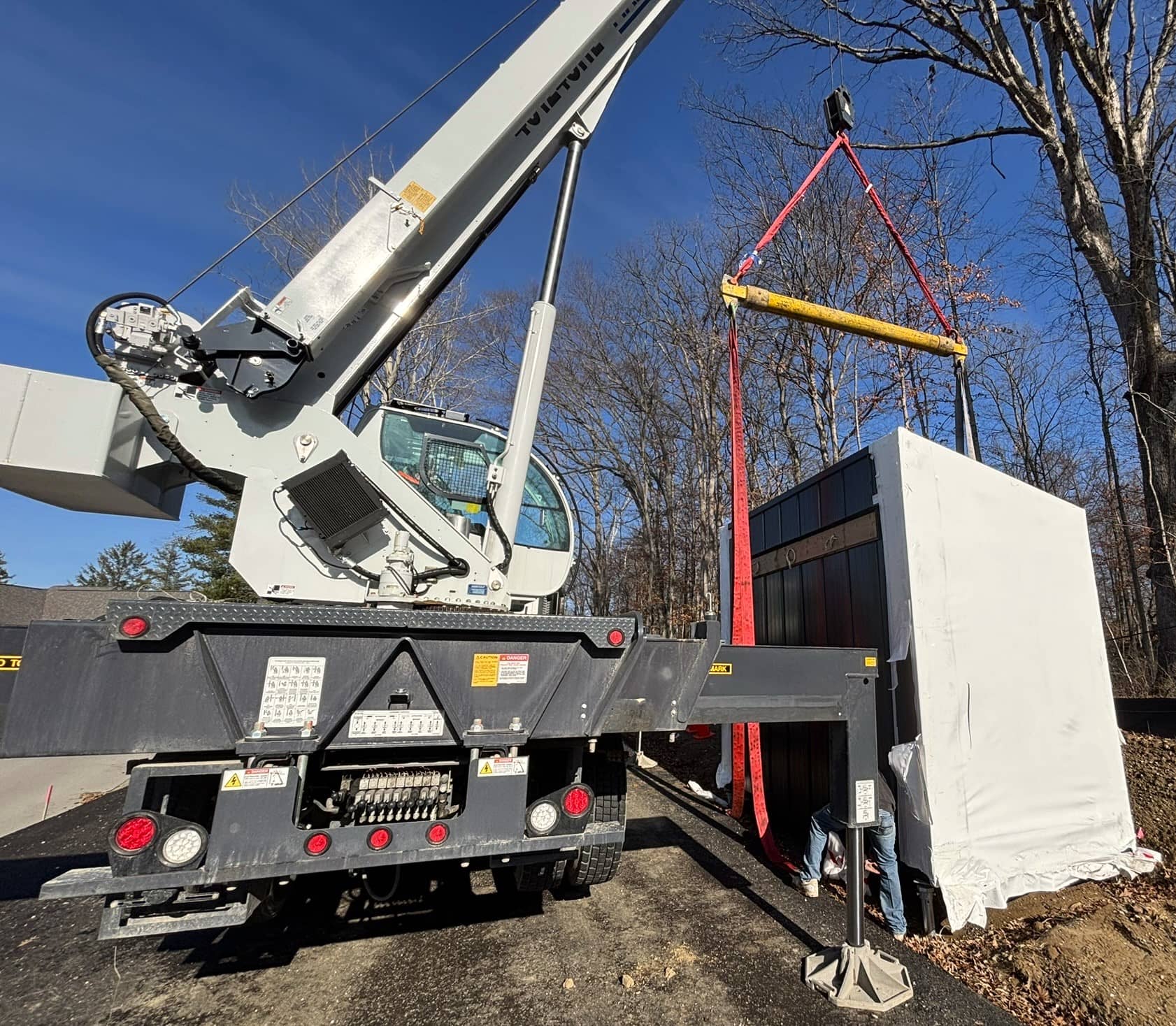 Crane operator and crew securing the prefabricated gatehouse to its foundation, surrounded by trees and construction equipment.